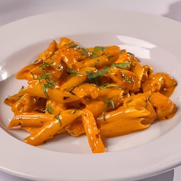 Penne pasta with creamy orange sauce and fresh green herbs on a white plate at Cafe Arrivederci.